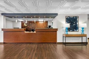 Un mostrador de recepción con detalles de madera, un diseño moderno de techo y un cuadro abstracto azul en la pared.