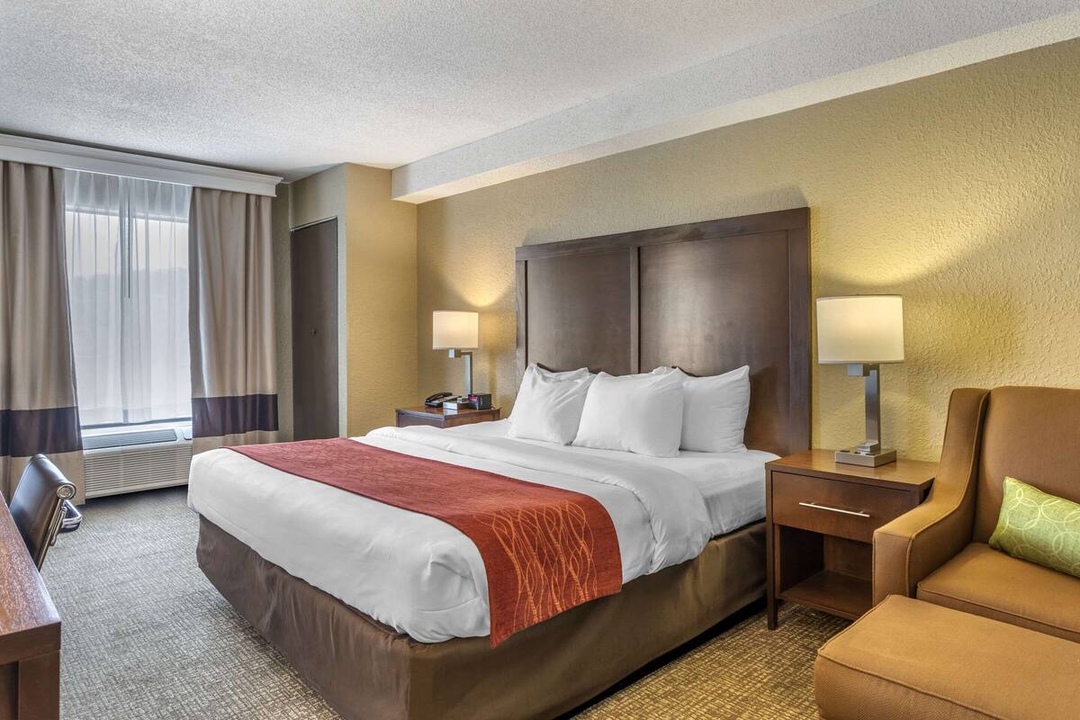 A hotel room with a large bed, two bedside tables with lamps, a chair, and a desk.