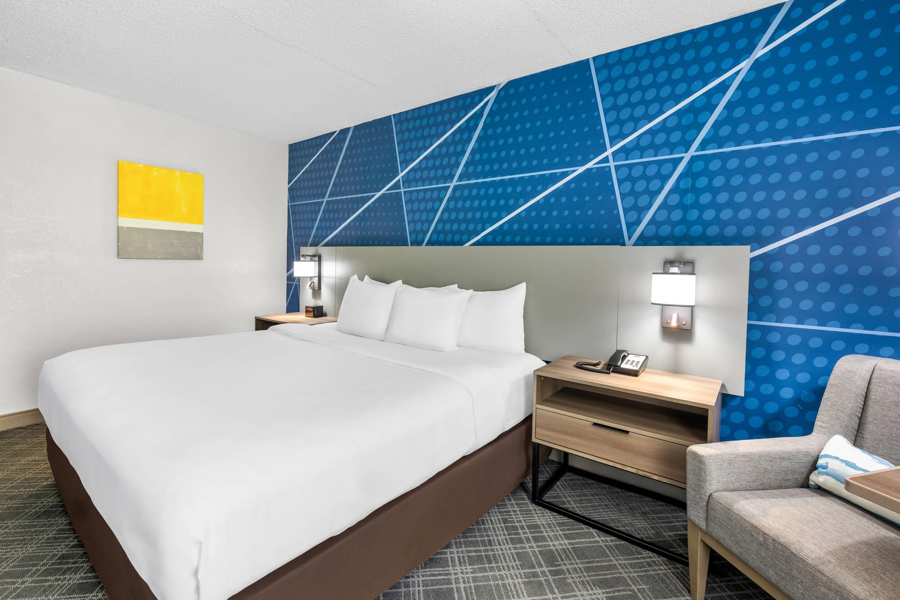 Habitación de hotel con una cama grande, un escritorio, una silla y una pared azul estampada.