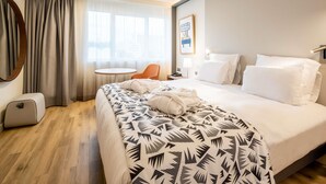 A hotel room with a bed, a round table, a chair, a desk with a lamp, and a wall-mounted light fixture.