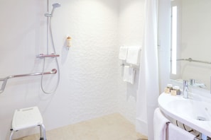 A bathroom with a shower, a white sink, a mirror, and a small white stool.