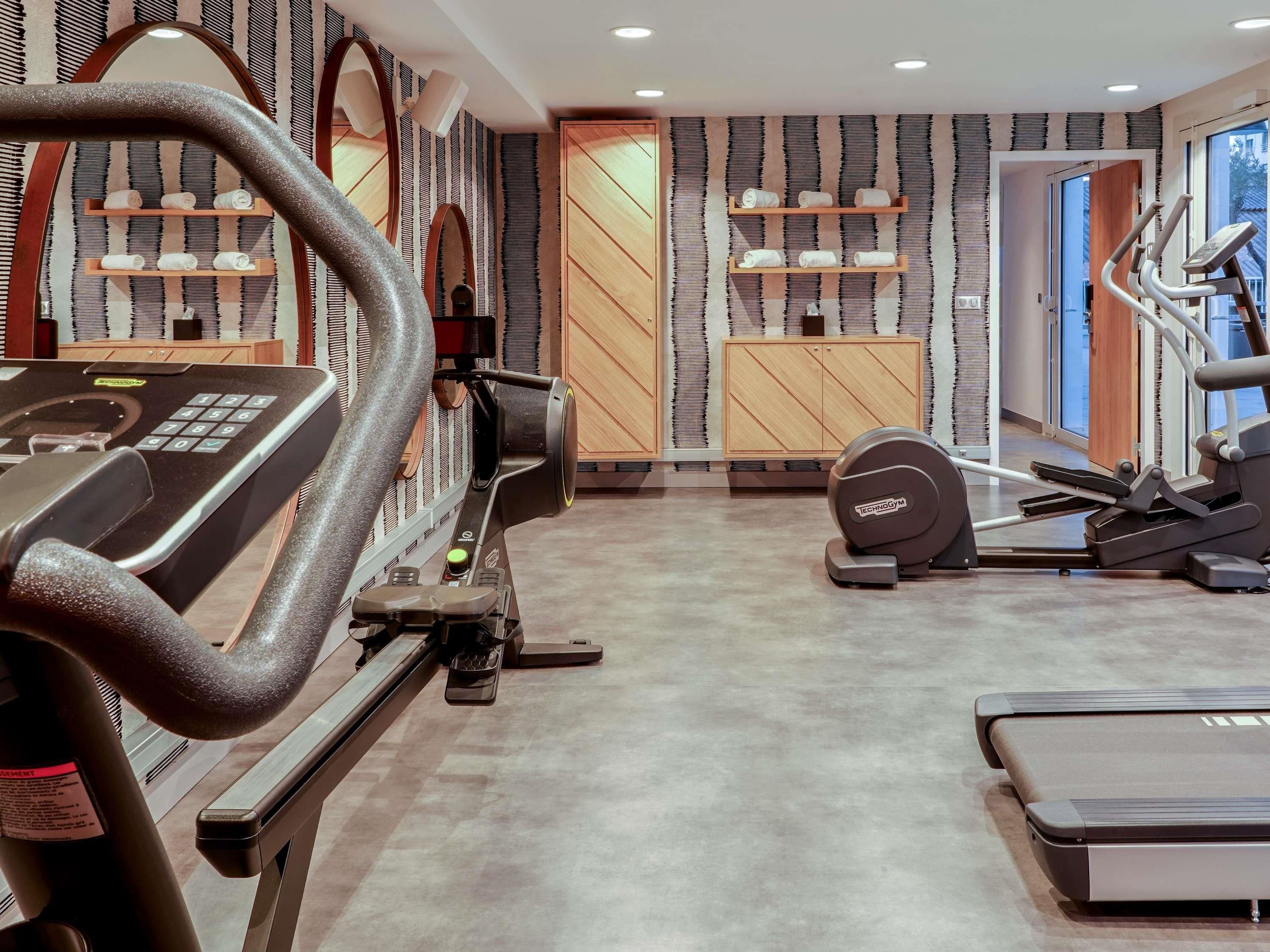 Un gimnasio con máquinas de cardio, bancos de pesas y una pared con estanterías que guardan toallas.