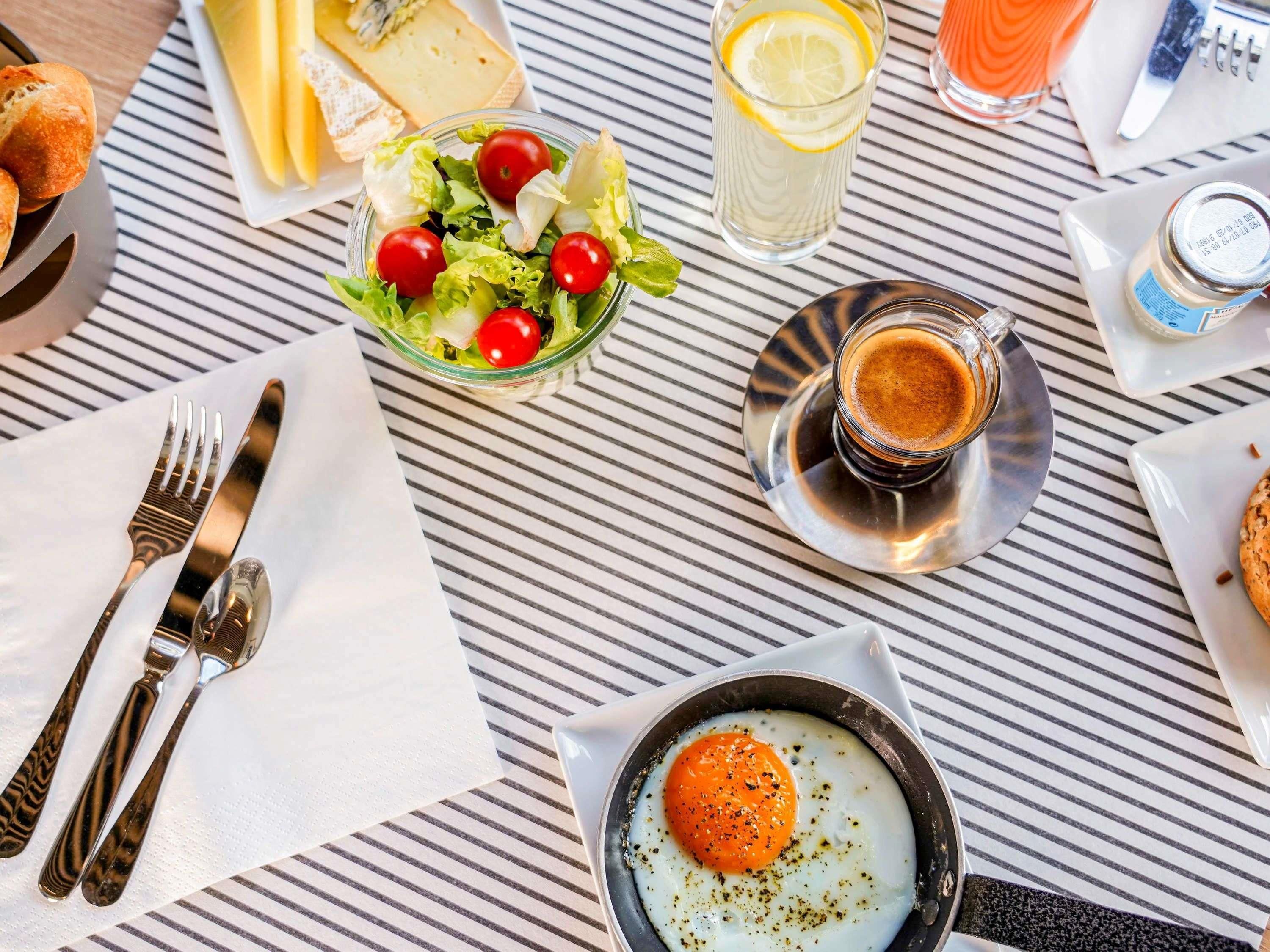 A breakfast setting with a plate of eggs, a glass of orange juice, a bowl of salad, and a cup of coffee on a striped table.