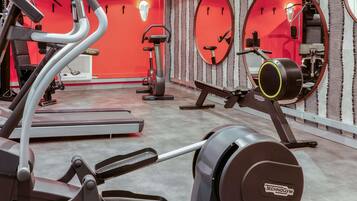 Ein Fitnessraum mit Cardiogeräten, Spiegeln und einer roten Wand.