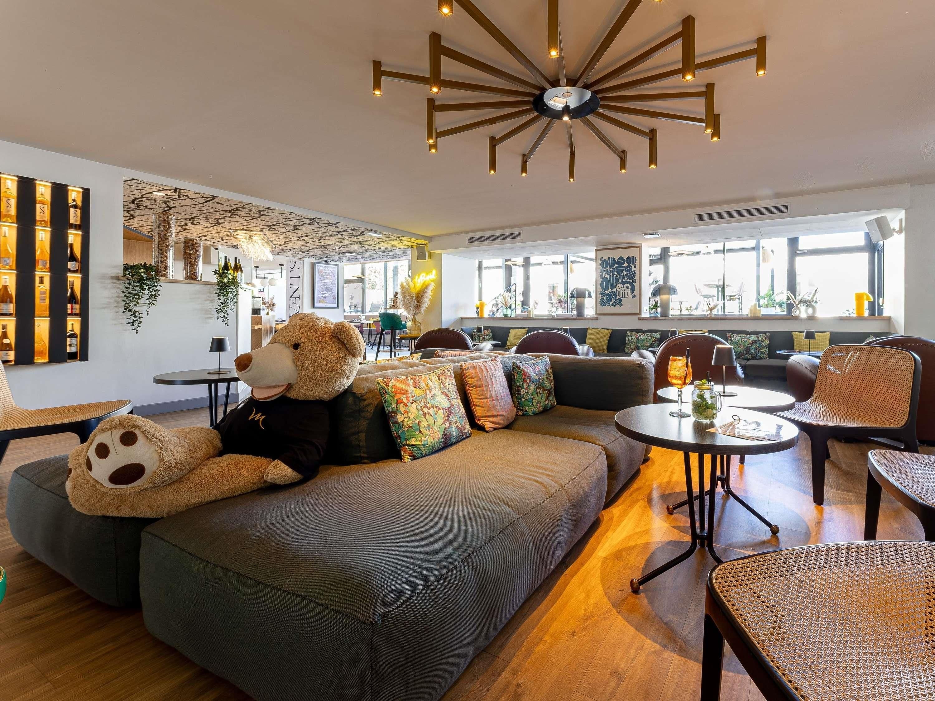 Ein stilvoller Aufenthaltsraum mit einer großen Couch, einem Teddybären und einer außergewöhnlichen Deckenleuchte.