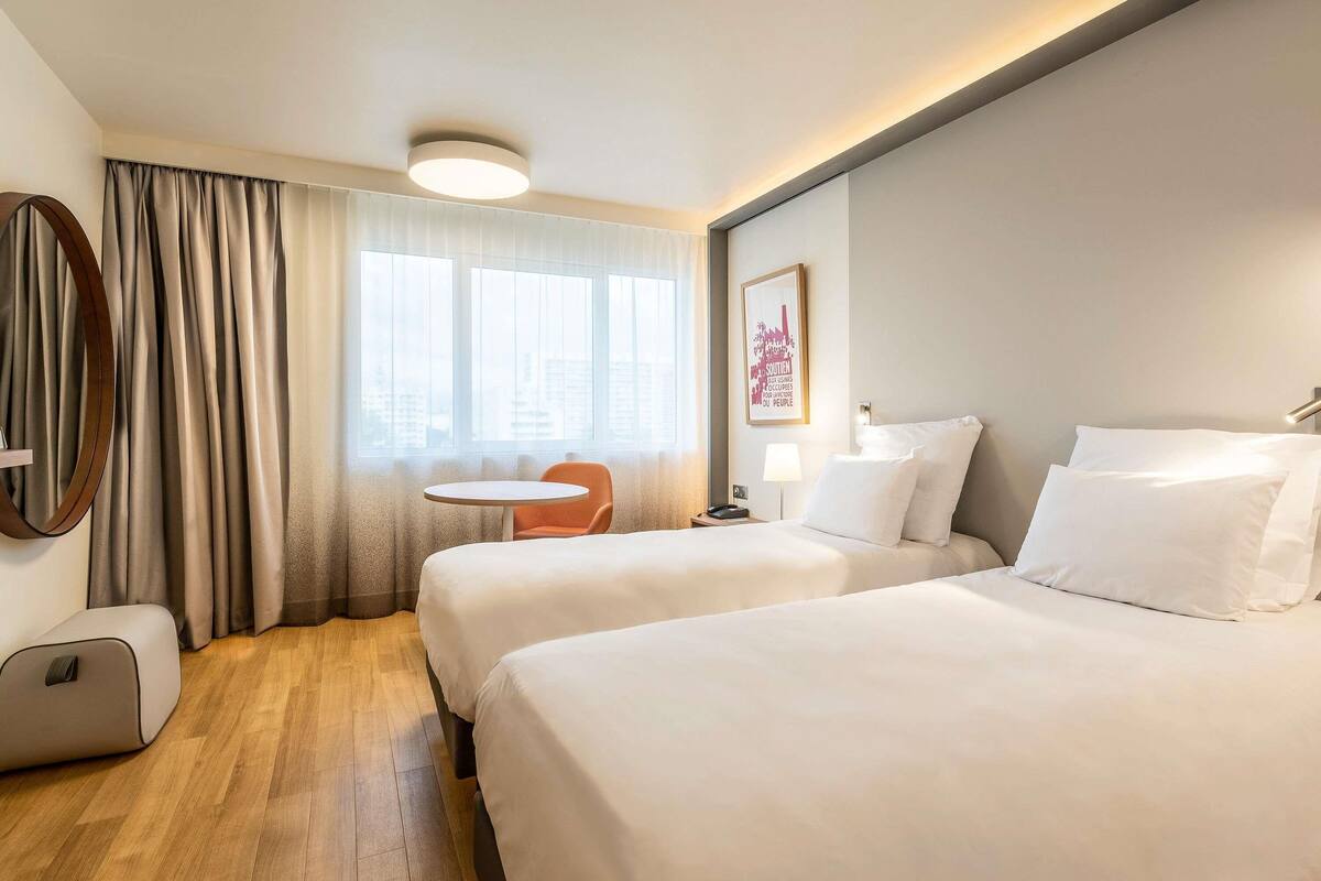 Une chambre d’hôtel avec deux lits, une table ronde, une chaise, une lampe et un tableau encadré au mur.