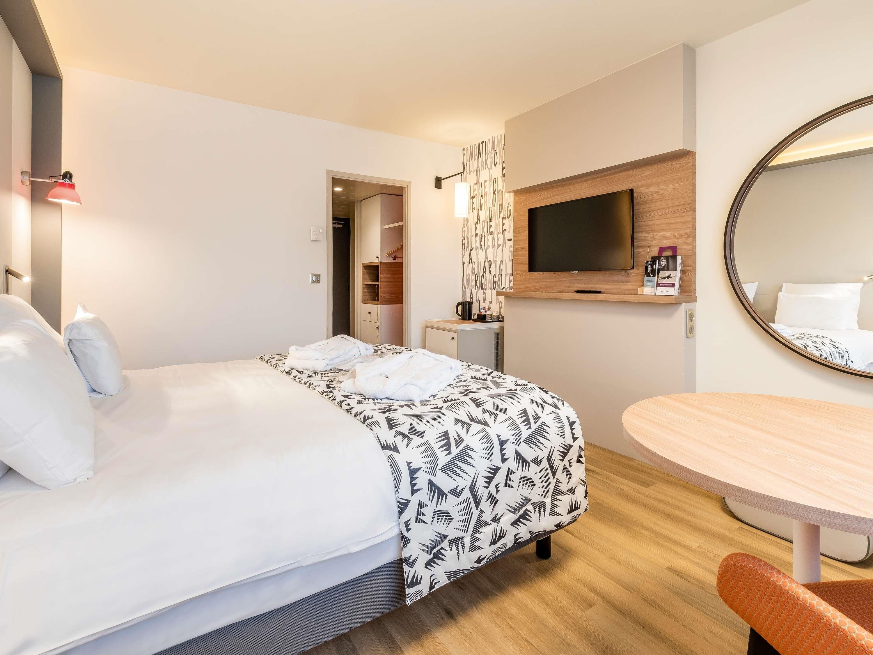 A hotel room with a bed, a desk, a television, and a mirror.