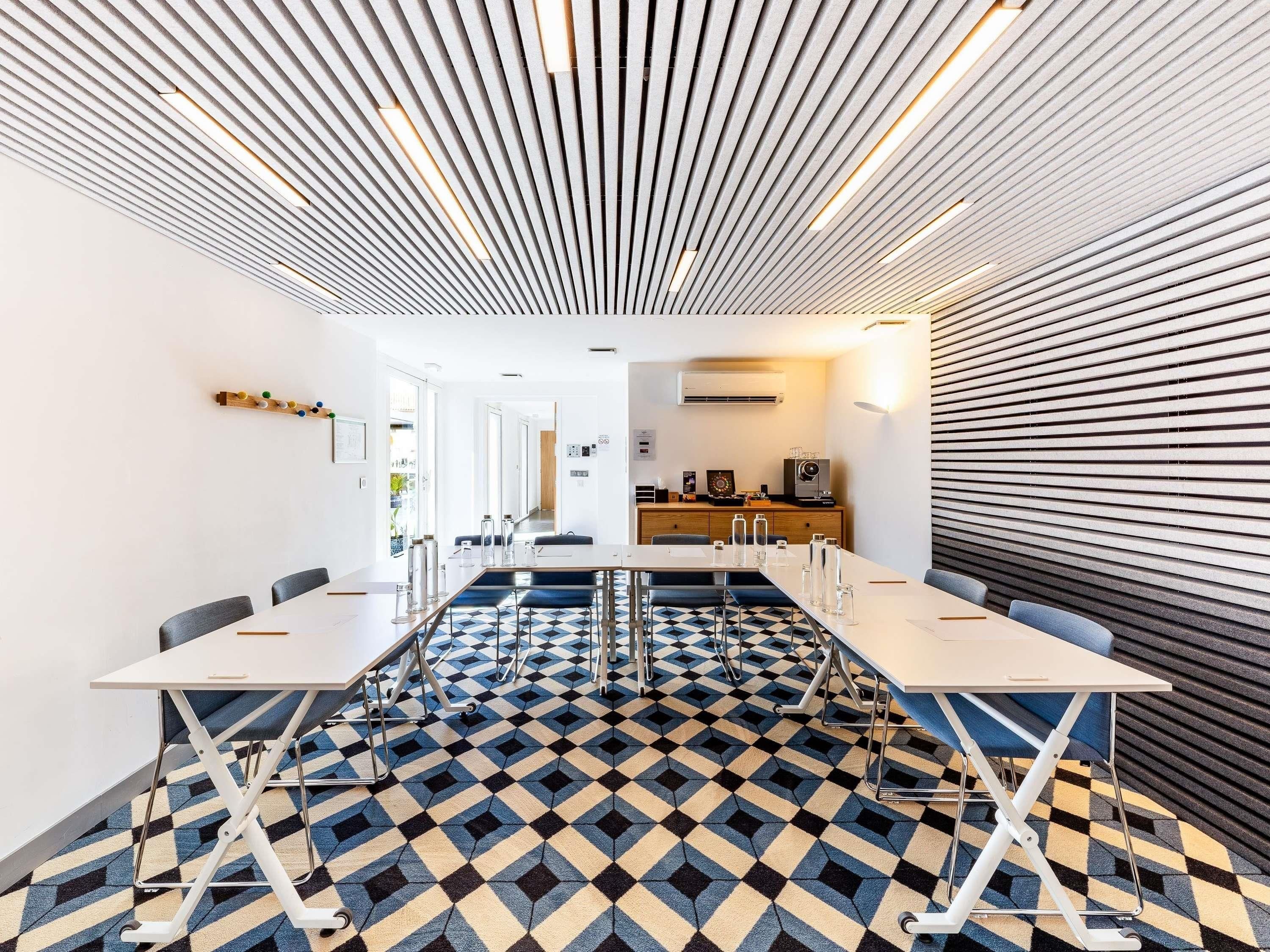 Een moderne vergaderzaal met een vloer met een geometrisch patroon, witte tafels en stoelen.