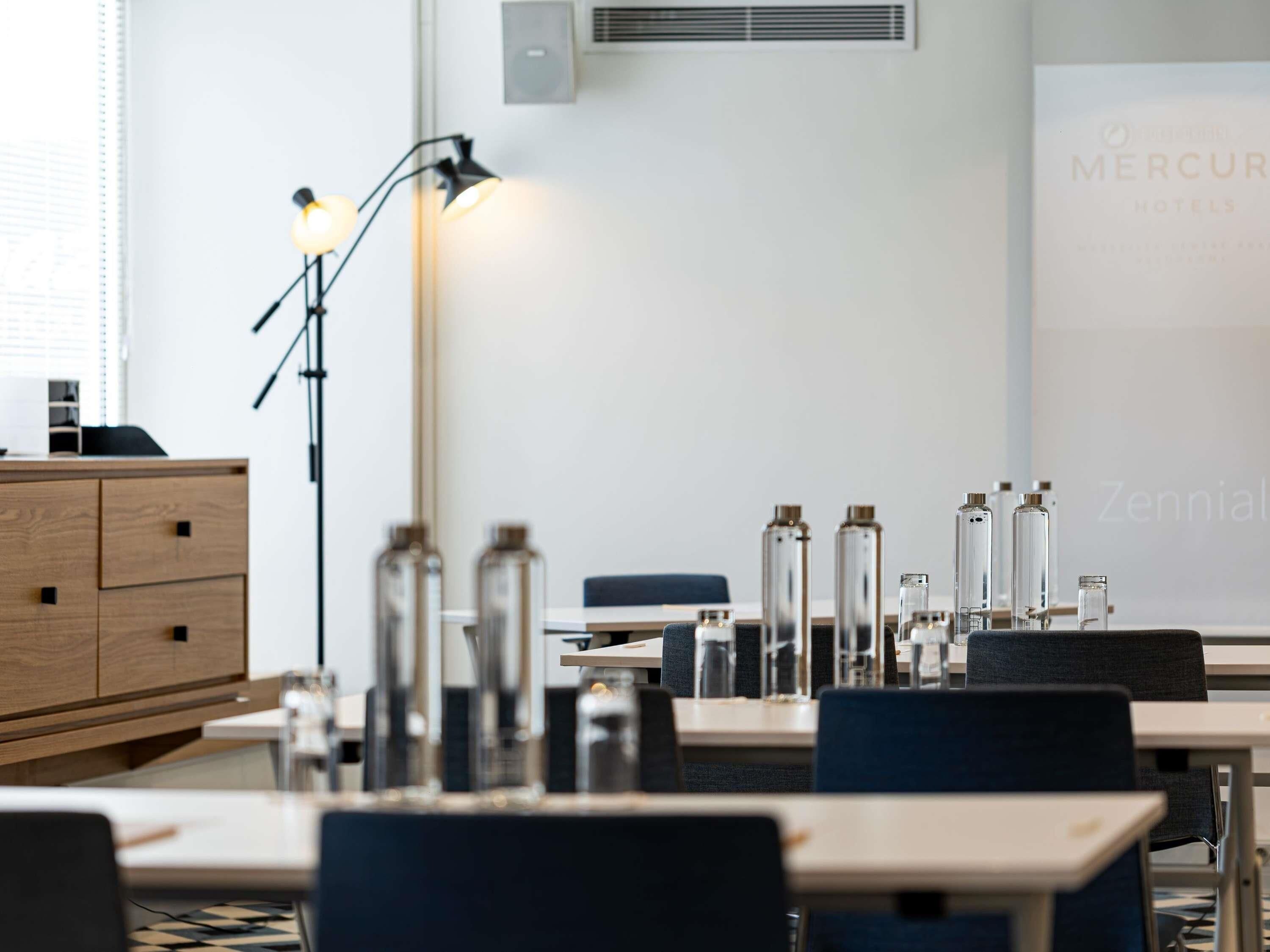 A modern hotel room with a desk, chairs, a lamp, and a minibar.