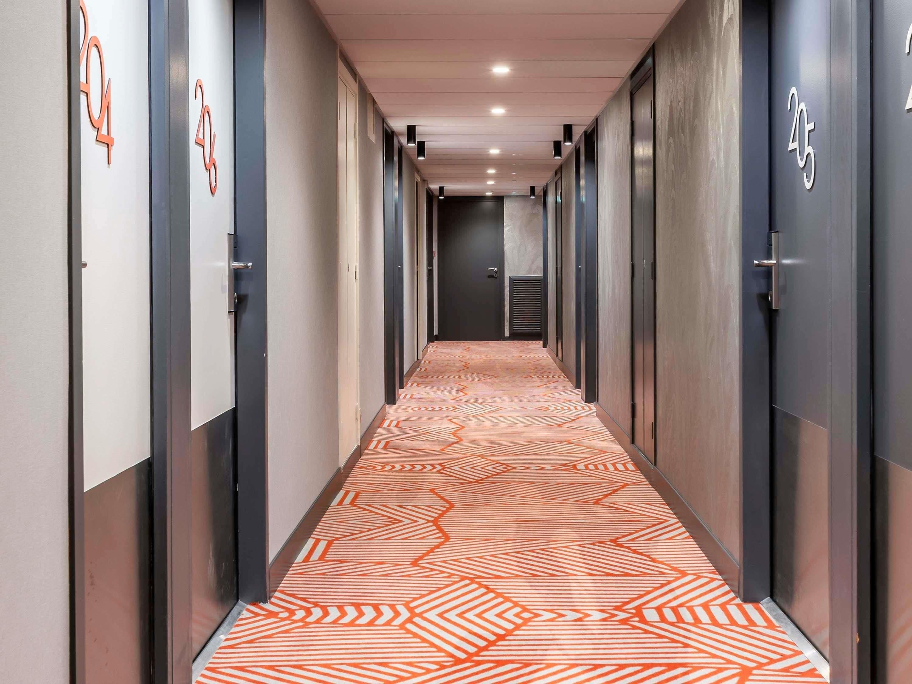 Un pasillo con puertas numeradas, un suelo con estampado y un techo con iluminación empotrada.