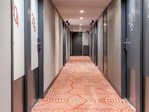 Un couloir avec des portes numérotées, une moquette à motifs et un plafond doté d’un éclairage encastré.