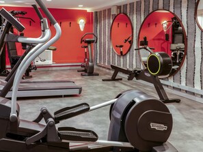 Een sportschool met cardioapparatuur, spiegels en een rode muur.