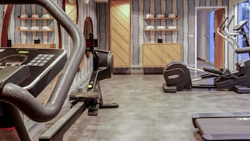 Un gimnasio con equipo de ejercicio, estantes de madera con toallas y una pared con estampado.