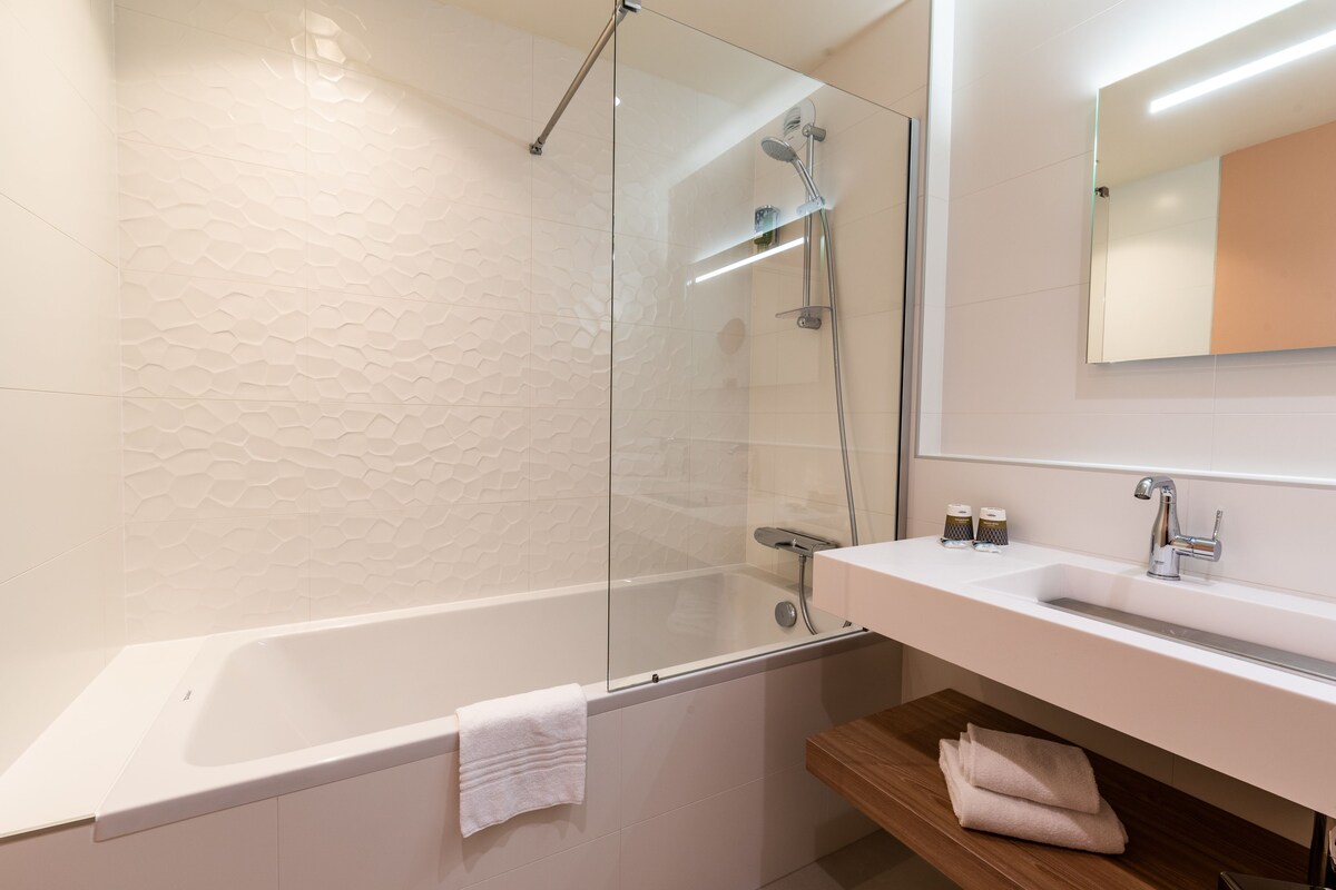 A modern bathroom with a glass-enclosed shower, a white bathtub, and a wooden vanity with a mirror.