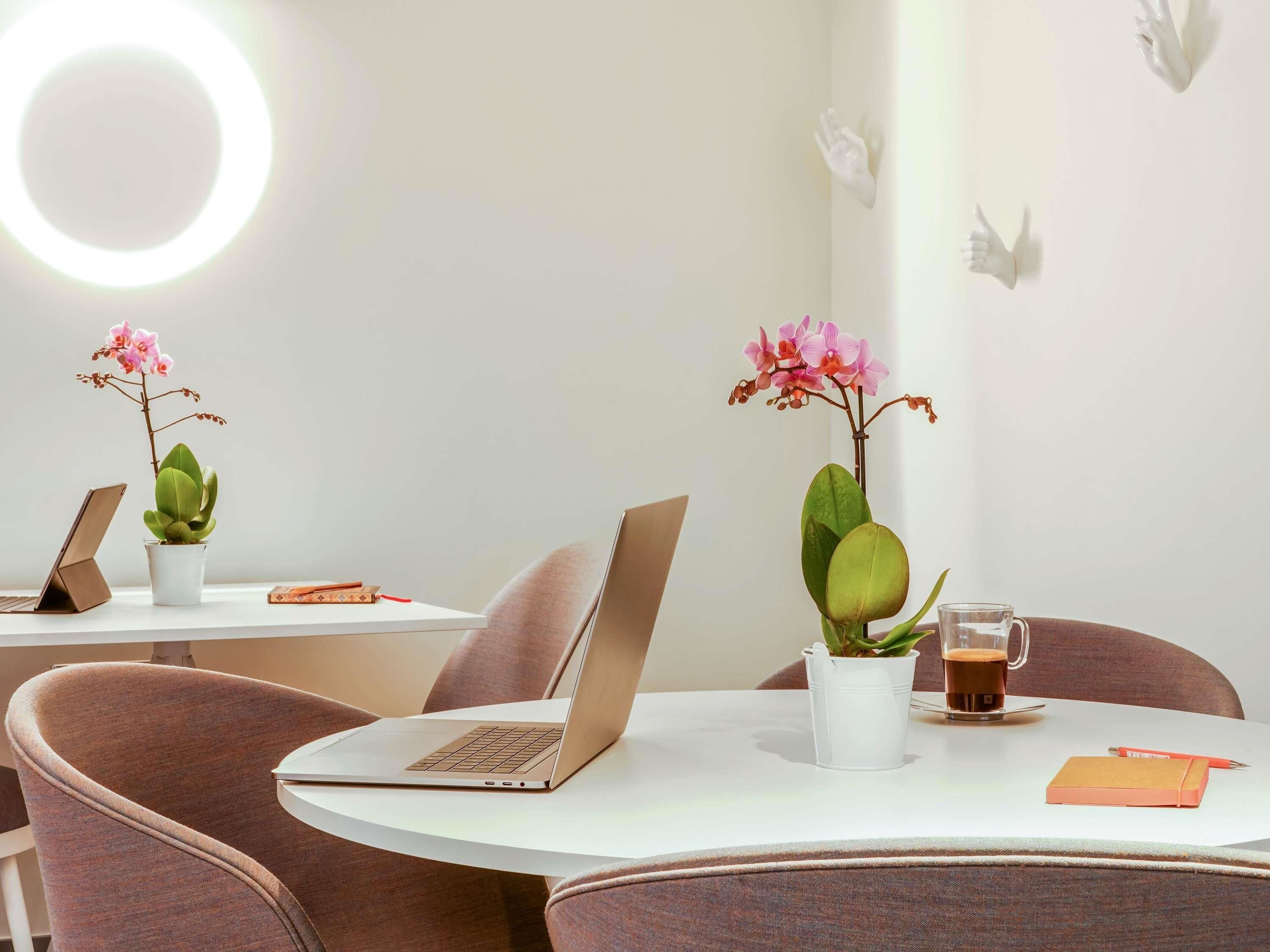 A modern workspace with two laptops on white tables, each accompanied by a potted plant and a cup of coffee.