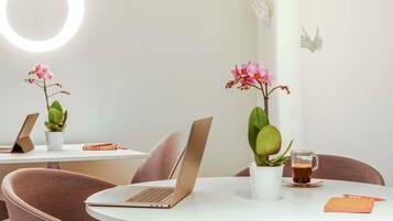 A modern workspace with two laptops on white tables, each accompanied by a potted plant and a cup of coffee.