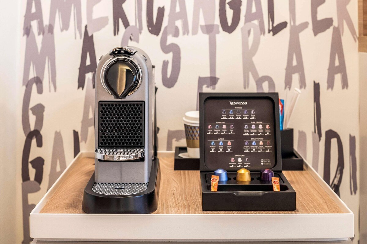 A Nespresso coffee machine and a coffee pod holder on a wooden table with a wall featuring large letters.