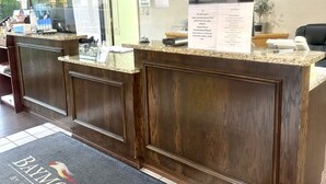 A reception desk with a dark wood finish, a glass partition, and a welcome mat with the logo "BAYLONT BY WYNDHAM".