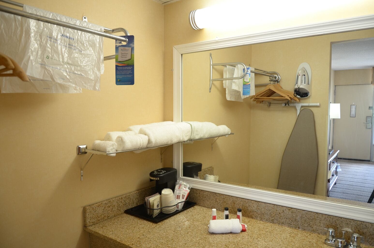 Een hotelbadkamer met een granieten aanrechtblad, een handdoekhouder met opgevouwen handdoeken, een spiegel en toiletartikelen.