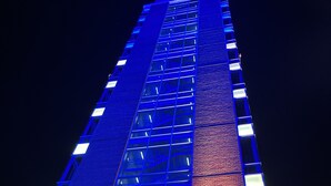 A tall building with a modern design, featuring a grid of windows and illuminated by blue and white lights.