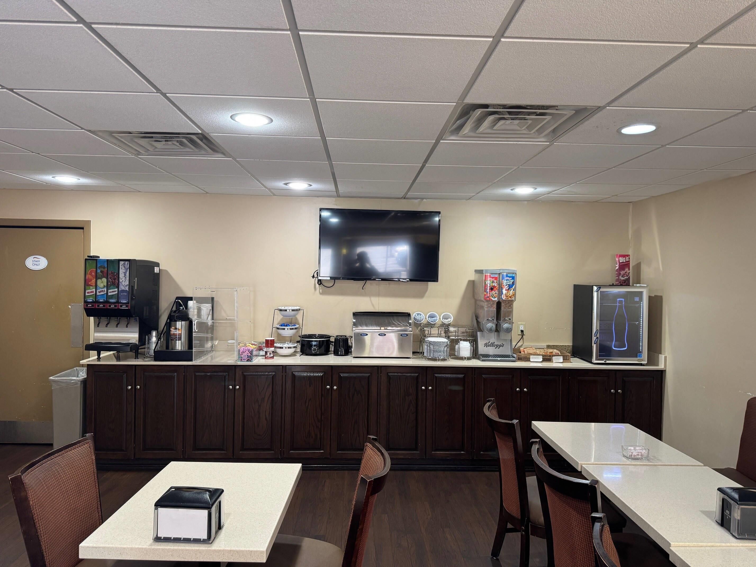 A hotel room with a kitchenette, a flat-screen TV, a coffee machine, and a refrigerator.