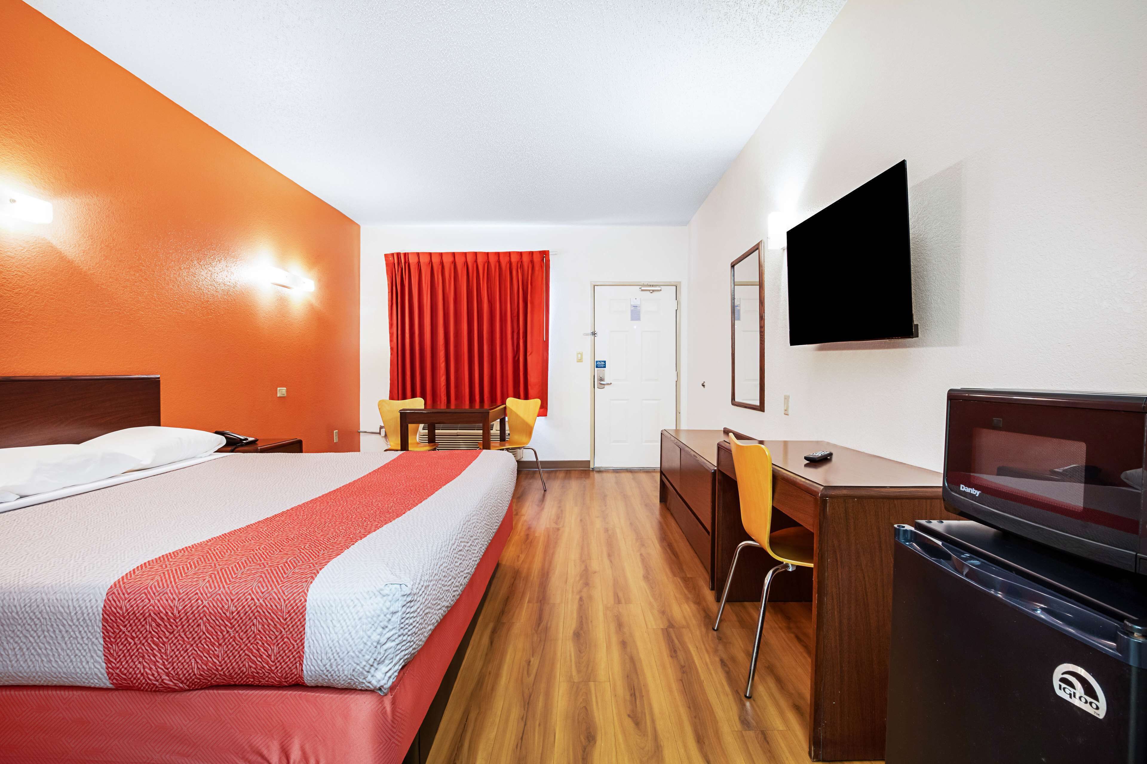 Habitación de hotel con cama, escritorio, silla, televisor y refrigerador.