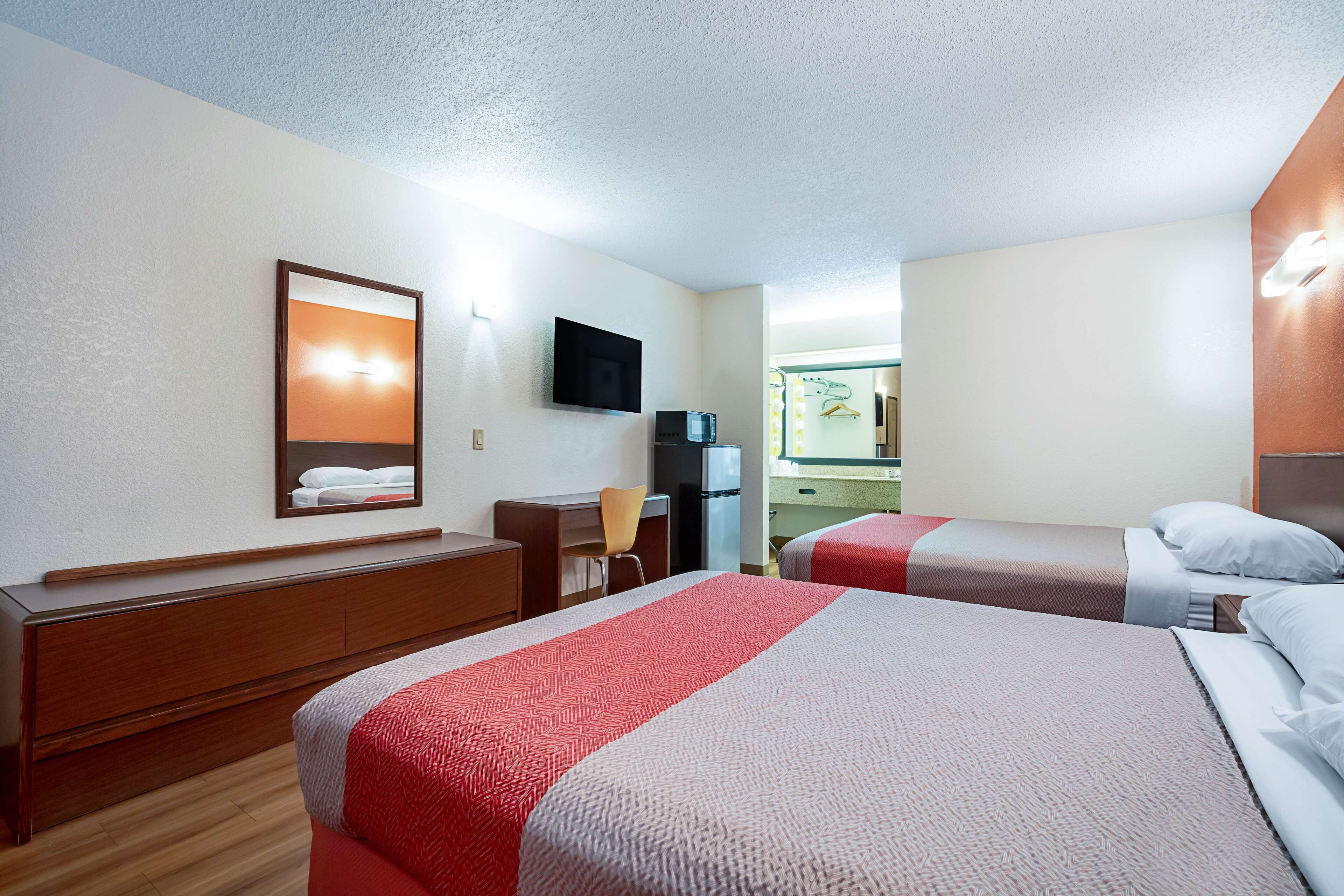 Una habitación de hotel con dos camas, un escritorio, una silla, un televisor y un espejo.