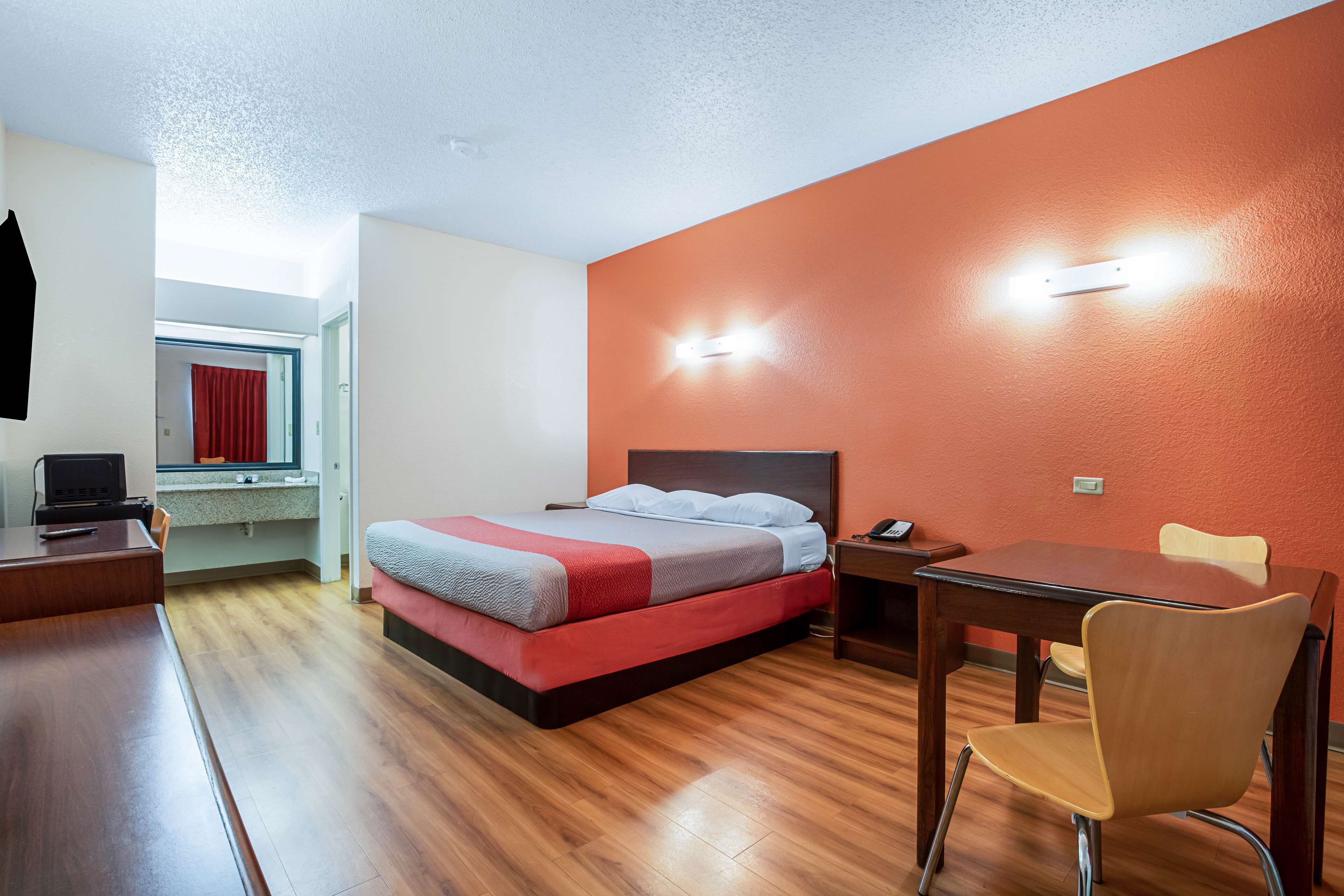 A hotel room with a bed, a desk, a chair, and a small table.
