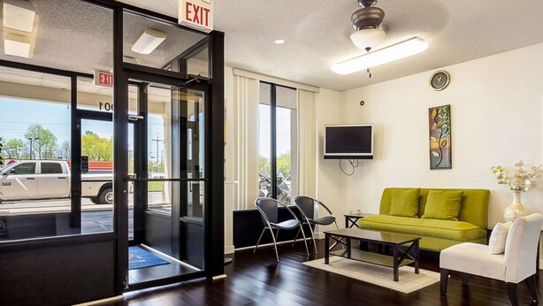 A hotel lobby with a green sofa, a white armchair, a coffee table, and a TV mounted on the wall. - Motel 6 Covington, TN (Covington)