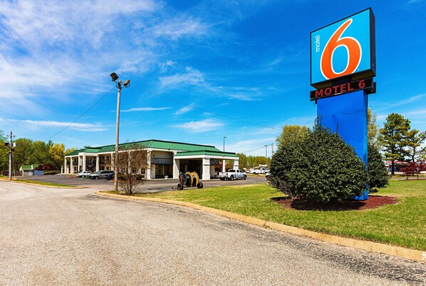 A motel with a large sign, a green roof, and a parking lot with several cars. - Motel 6 Covington, TN (Covington)