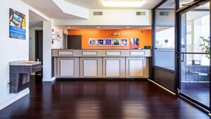 A reception area with a wooden floor, a counter with a glass door, and a wall with framed pictures and a sign. - Motel 6 Covington, TN (Covington)