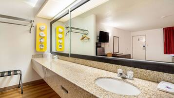 A bathroom with a granite countertop sink, a mirror, a towel rack, a hand dryer, and a shower area.