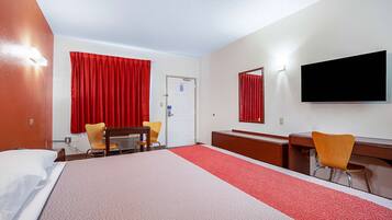 A hotel room with a large bed, two chairs, a desk, a flat-screen TV, and a red curtain.