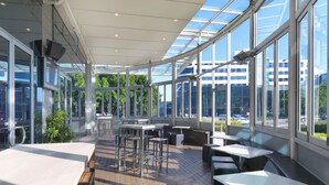 Een modern, open café met grote ramen, houten vloeren en verschillende zitplaatsen, zoals tafels en banken.