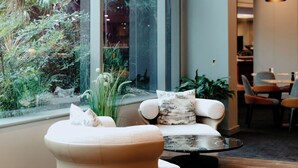 Een modern interieur met een groot raam, een zithoek met een ronde tafel, en een eethoek op de achtergrond.