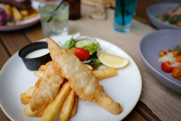 A plate of fish and chips with a side of salad and a small bowl of sauce.