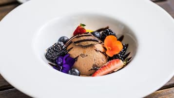 A dessert with chocolate ice cream, strawberries, blueberries, blackberries, and a flower on a white plate.