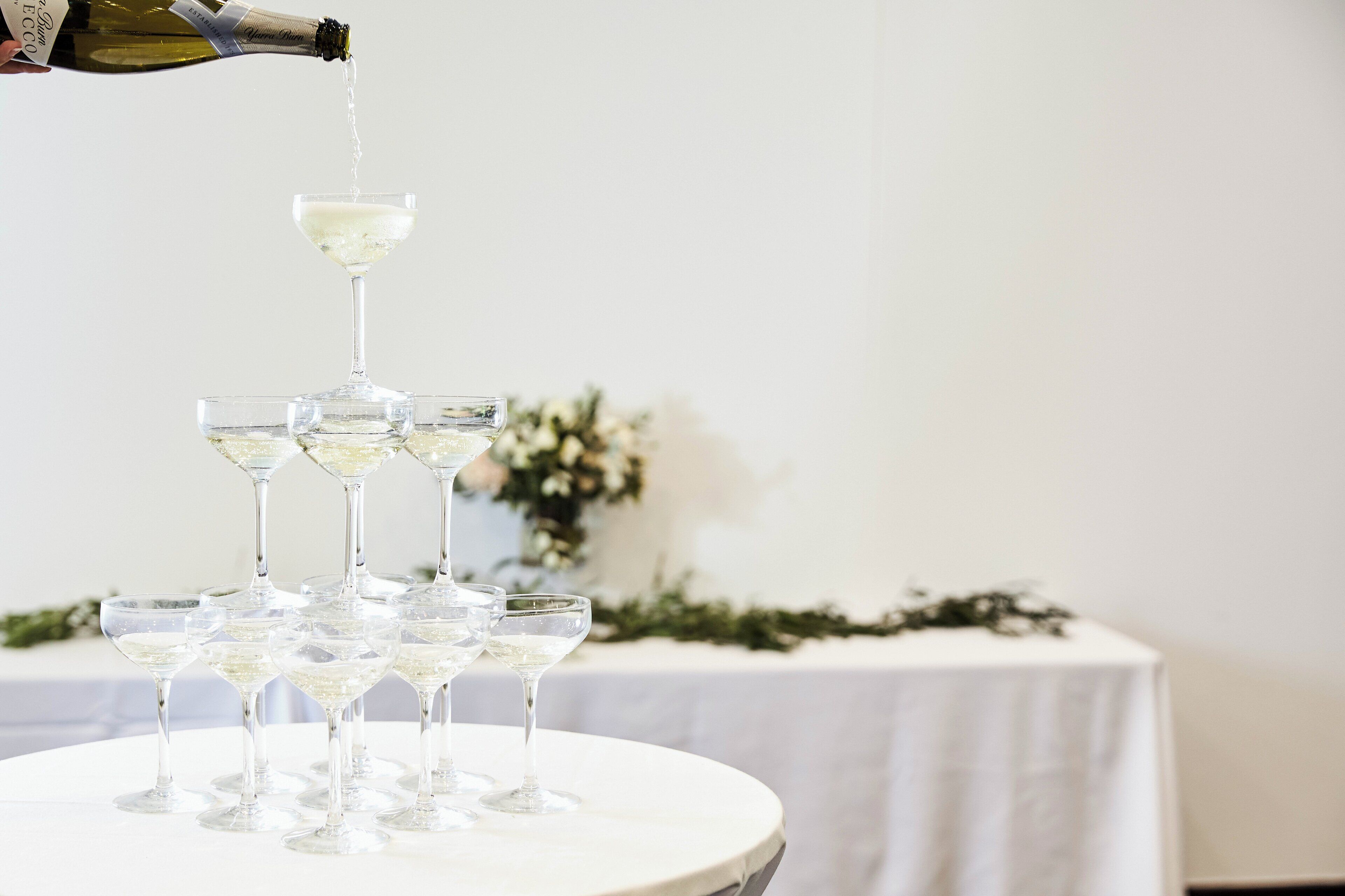 A table with multiple champagne glasses arranged in a pyramid, with a bottle being poured into the top glass.