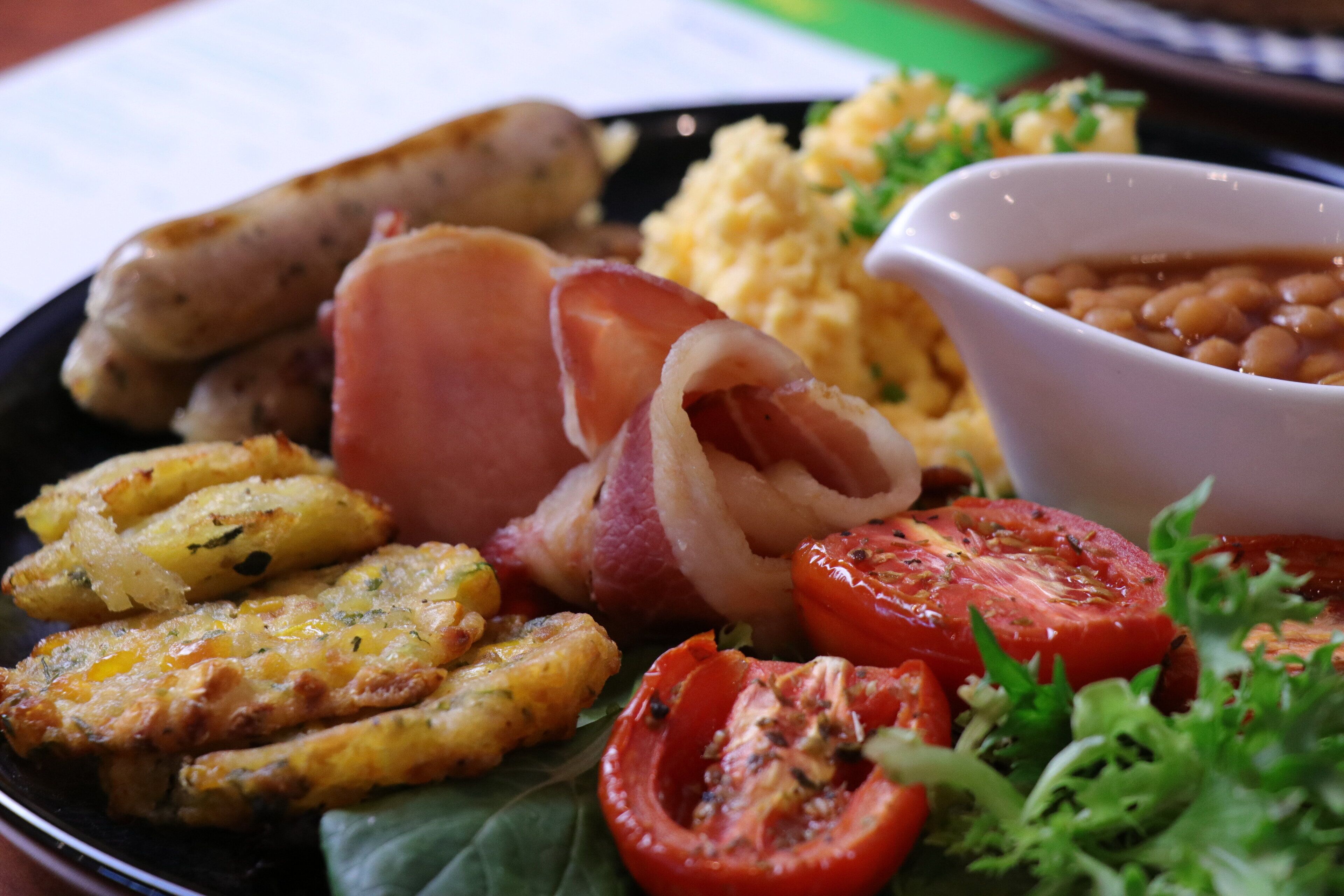 A plate of food including sausages, bacon, scrambled eggs, beans, and tomatoes.