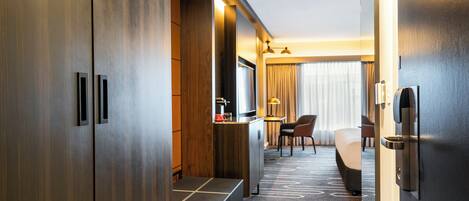 A hotel room with a large wardrobe, a desk with a lamp, a bed, and a chair.