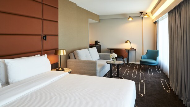 Una habitación de hotel con una cama grande, un sofá, una mesita con lámpara y una silla.
