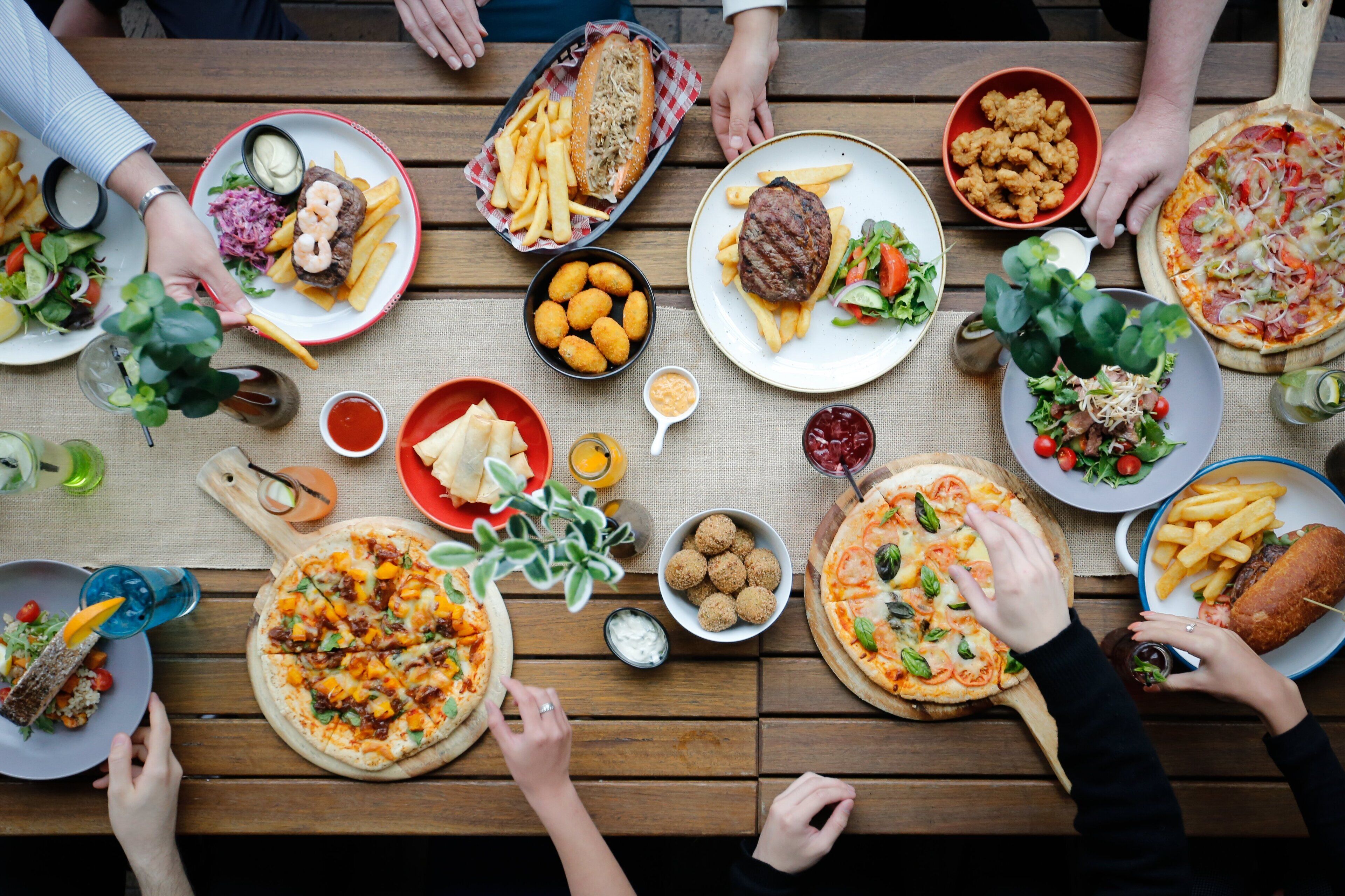 A wooden table with various dishes including pizzas, salads, and bread.