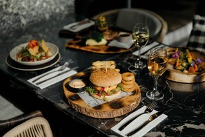 A dining table with a variety of dishes, including a burger, fries, and salad, along with wine glasses and cutlery.