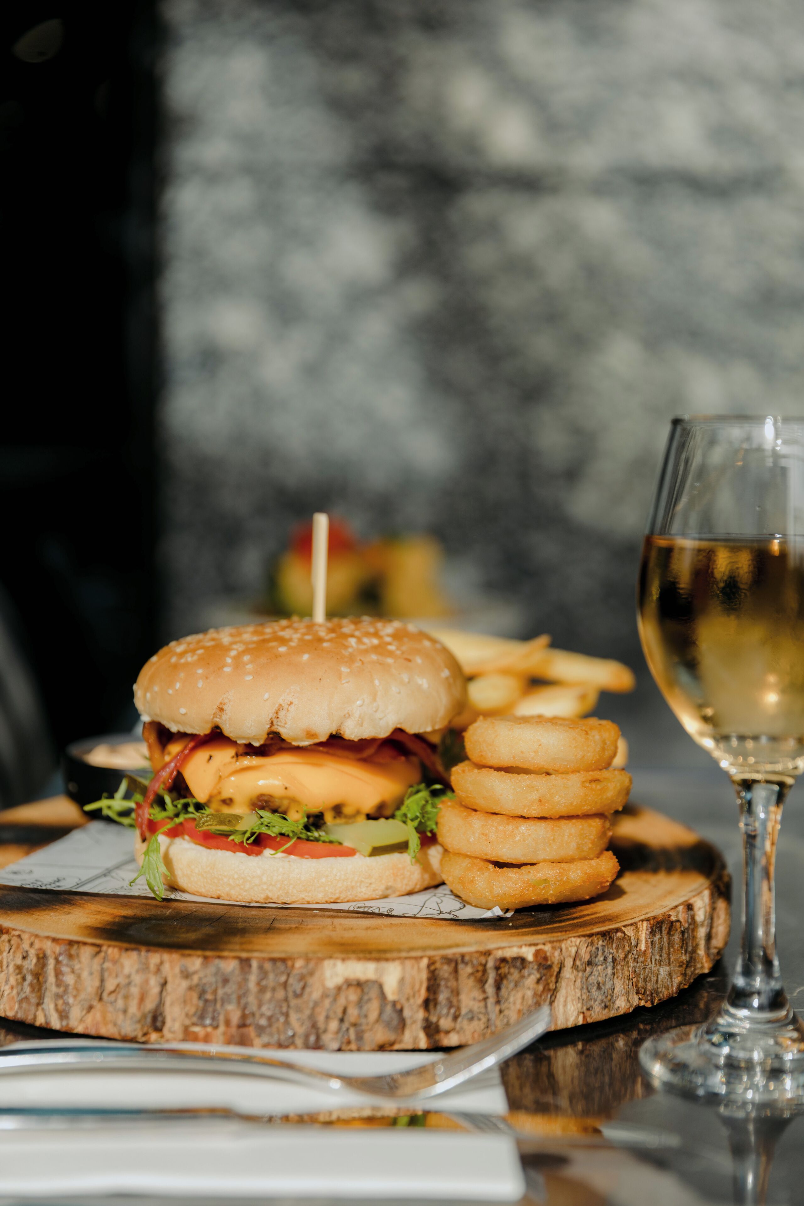 Una comida con una hamburguesa, papas fritas y una copa de vino blanco sobre una tabla de madera.