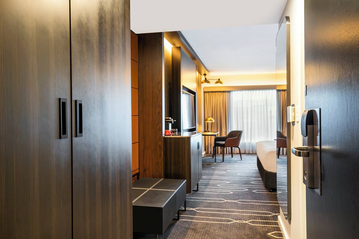 Une chambre d’hôtel avec une grande armoire, un bureau avec une lampe, un lit et une chaise.