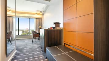 A hotel room with a large window, a seating area with a sofa and chairs, and a small kitchenette.