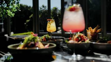 A table set with various dishes and drinks, with a view of trees and a building in the background.