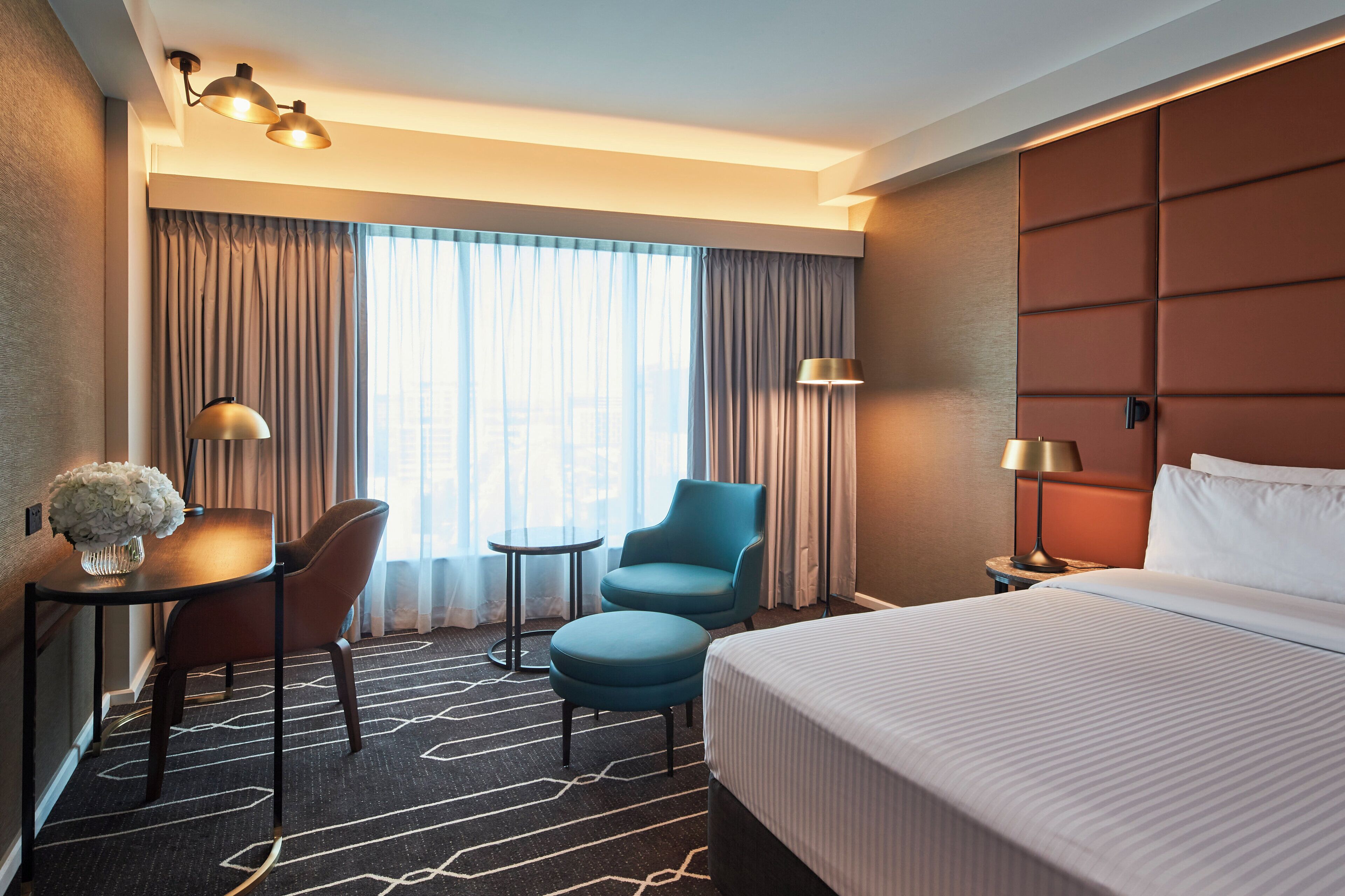 Una habitación de hotel con una cama grande, un escritorio con lámpara, una silla y una mesita.