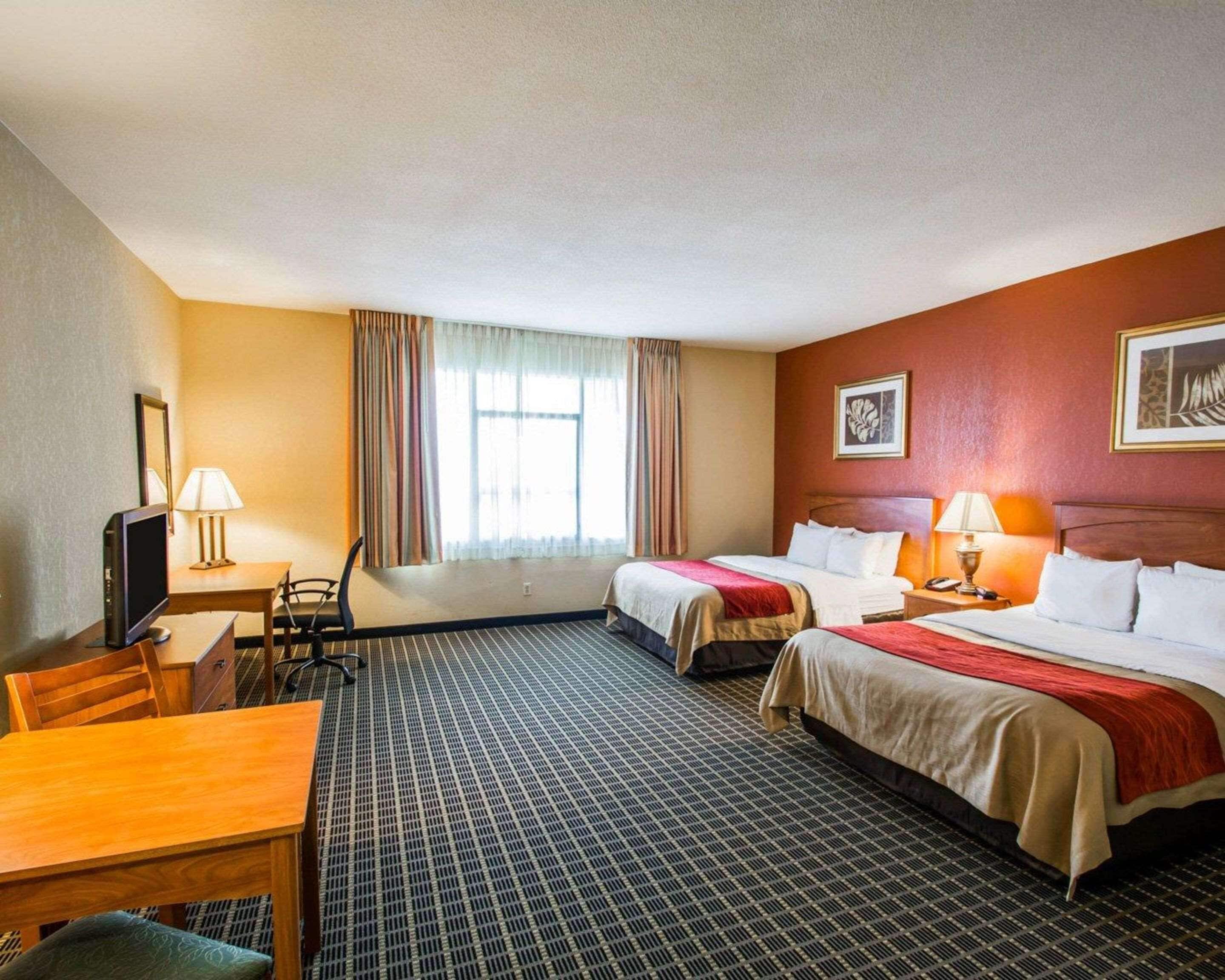A hotel room with two beds, a desk with a chair, a television, and a window with curtains.