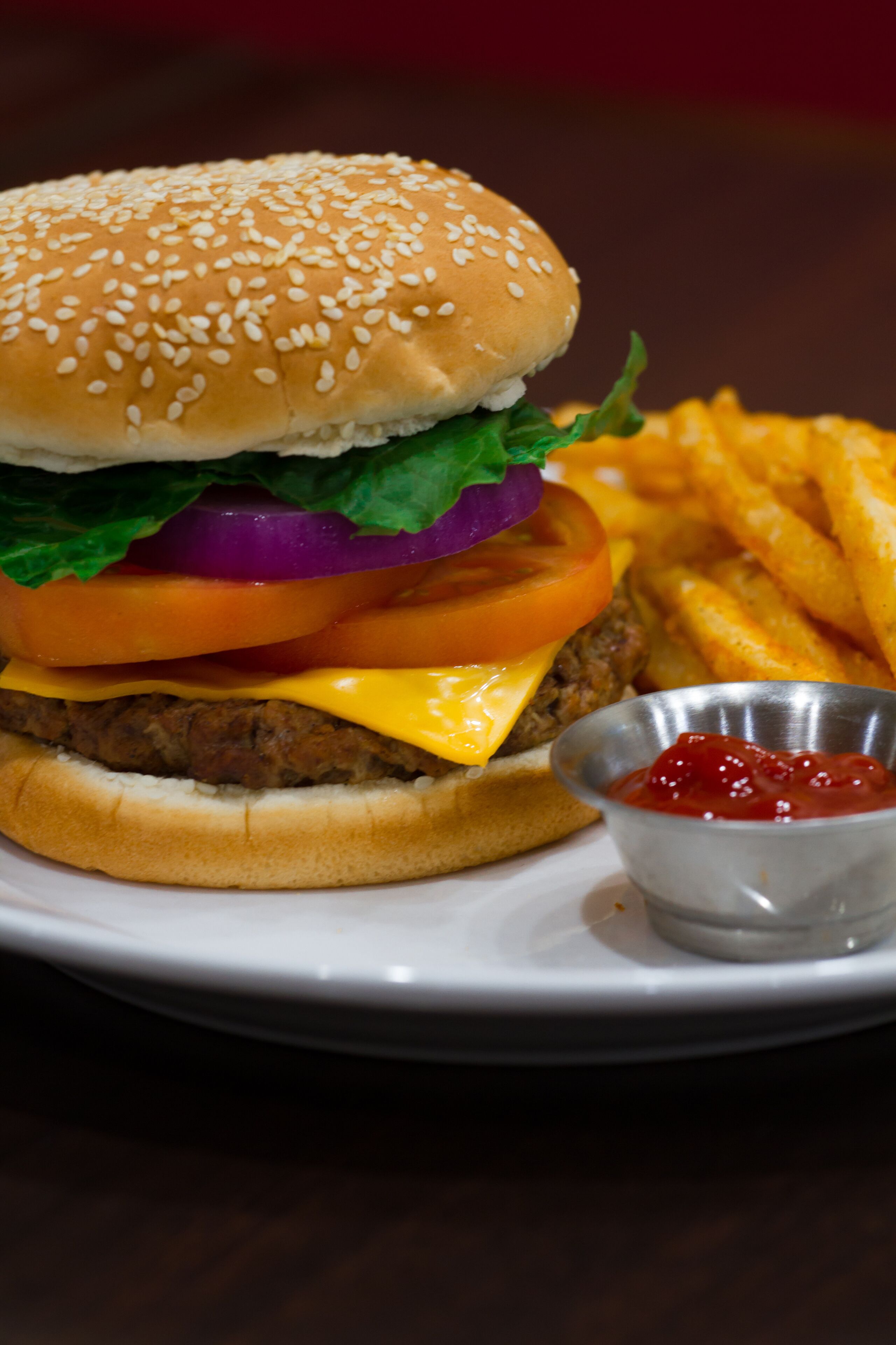 A hamburger with lettuce, tomato, and cheese, served with French fries and a small container of ketchup.